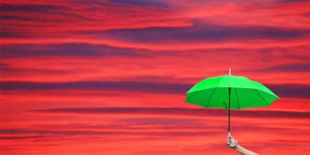 A man holding green umbrella in front of red sky and clouds background at sunsetの写真素材