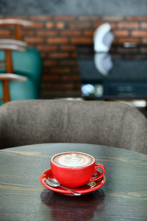 Red cup of coffee latte plant shape on old wooden background with blurred oom in the restaurantの写真素材