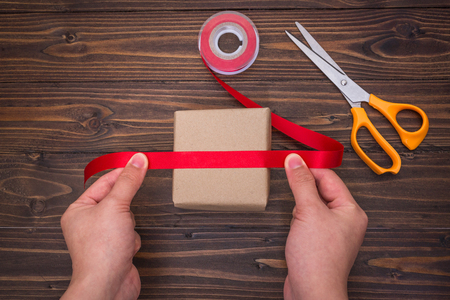 Female hands making of handmade gift box with red ribbon and scissorsの写真素材