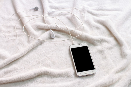 white mobile phone with headphones on a towel
