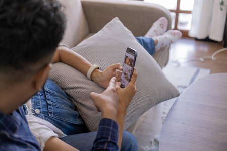 Smiling couple embracing while looking at mobile phone, Loving couple relaxing on sofa.の写真素材