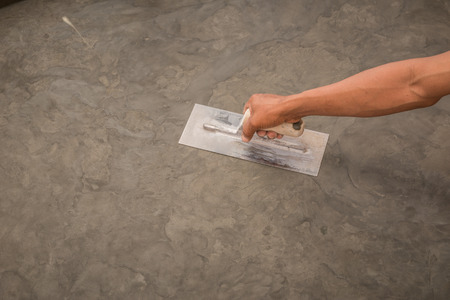 Close up of hand using steel trowel to finish wet concrete floor of polished concrete surface