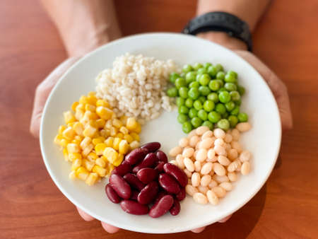 top view of navy bean and red bean and corn and  green peas and millet in white plate on hand and wood table backgroundの写真素材