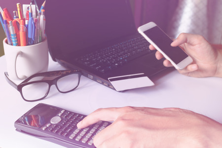 Man using calculator and holding smart phone for online payment with card on blank laptop screen on...