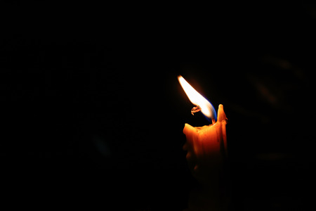 One light candle burning brightly, image is isolated against a black background and fades into a...