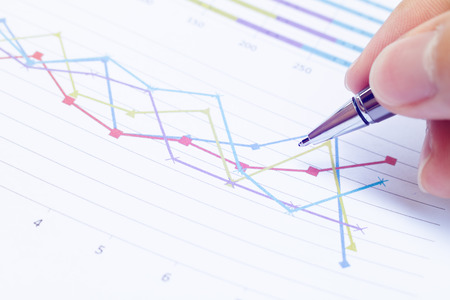 Close up Businessman hand holding pen and thinking about problem with business chart on table...