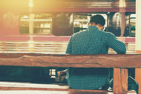 Young asian man sitting with listening music and waiting train at station.の写真素材