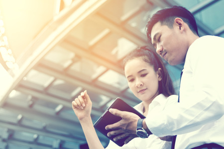 Two asian business standing under office company building with looking information financial on tablet screen and searching data result.の写真素材