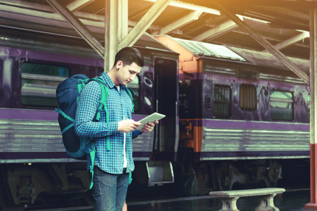 Hipster smart man with looking tablet screen waiting at train station.の写真素材