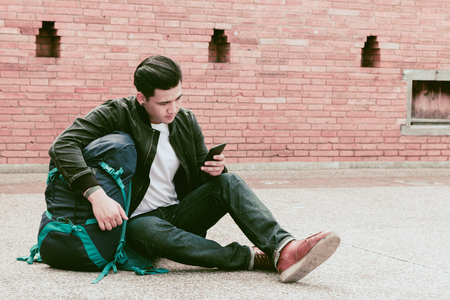 Asian traveler man sitting on the street and using smartphone.の写真素材
