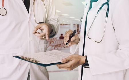 Medical colleagues holding clipboard with paper and working together in doctors office