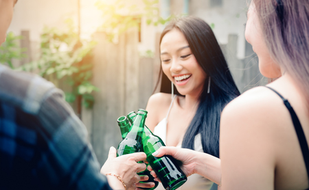 Young asian people holding beer bottles and clink with drinking together.の写真素材