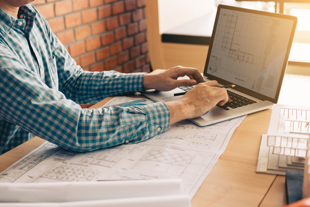 Architect sitting in modern office using computer working project and looking blueprint on screen.の写真素材