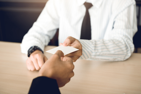 Two businessmen exchanged white business cards on a wooden table in office.の写真素材