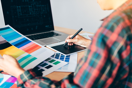 Freelance creative designers working on desk using digital graphic tablet and drawing with pen in...