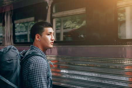 Young asian hipster man standing and waiting train on platform.の写真素材