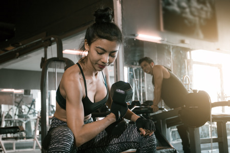 Asian woman lifting dumbbell at gym and man is peek her.の写真素材