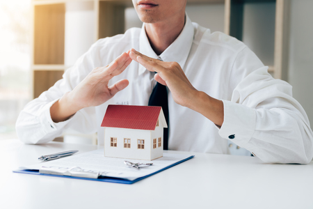 Hands covering or protective miniature model house on table with key and contract paper about insurance concept.の写真素材