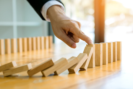 Close up finger businessman stopping wooden block from falling in the line of domino with risk concept.の写真素材