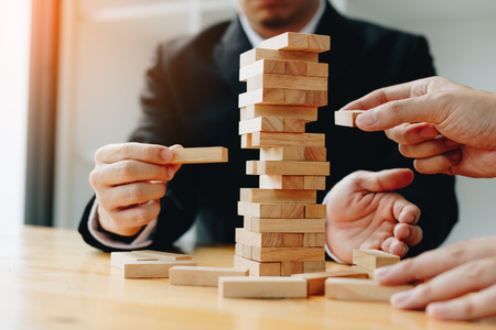 Two businessmen help to hold the wood block to fall down.の写真素材