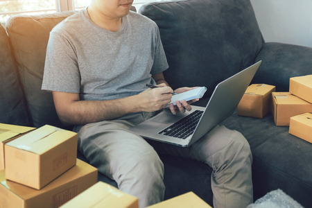 Young asian man looking on computer laptop and writing order list on paper, SME concept.