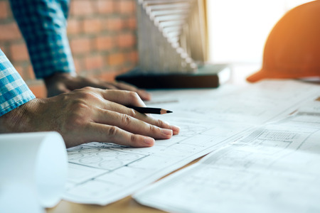 Hand of young engineering man drawing on blueprint with model on desk.