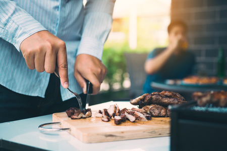 Asian friends are using a knife and a fork to cut the grilled meat on the chopping board to bring food together with friends celebrate with fun.の写真素材