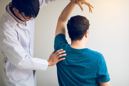 Chiropractor stretching a young man arm in medical office