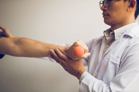 Asian physiotherapist helping a patient lifting dumbbells work through his recovery with weights in clinic room.の写真素材