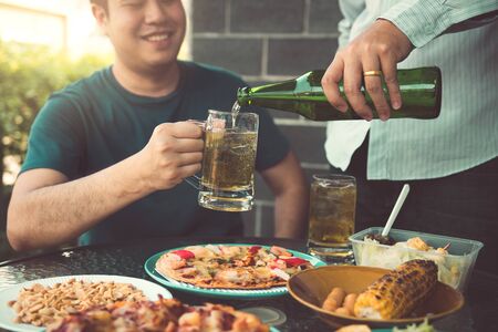 Asian friends are helping to pour beer into the bottle of his partner and have fun together in celebration.の写真素材