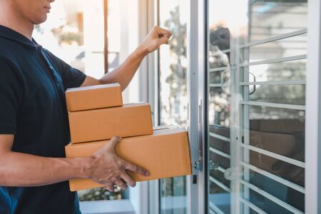 Young asian courier is using the hand of the knock at the door to deliver the goods.の写真素材