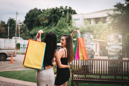 Rear view with two beautiful asian woman holding shopping bag at shopping market outdoor.の写真素材