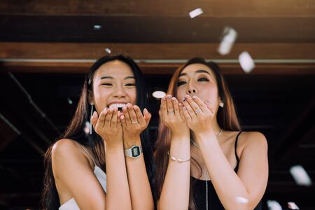 Two asian women blowing paper confetti for a celebration in his home.の写真素材
