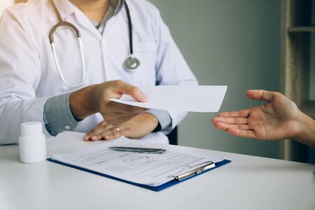Asian male doctor talking in clinic room and handing a prescription to the patient.