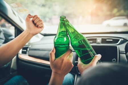 Two male friends are celebrating in the car while they are clinking beer bottle together.
