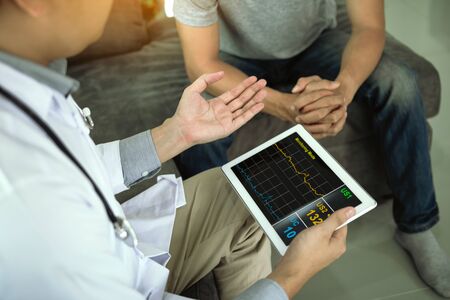 Asian doctor visited the patient at home while using the tablet explaining the patient condition and...