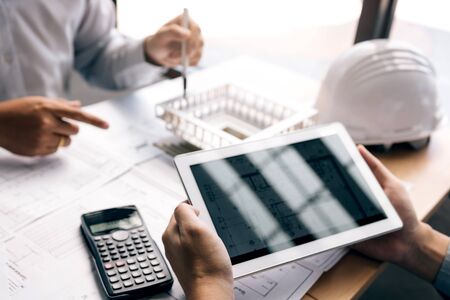 Two engineering working together and using digital tablet looking blueprint and analysis with...