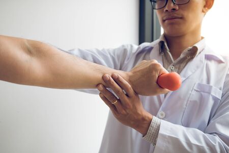 Asian physiotherapist helping a patient lifting dumbbells work through his recovery with weights in clinic room.の写真素材
