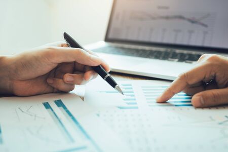 The accounting staff of the company are jointly analyzing the graph of the expenses on the desk in the office.の写真素材