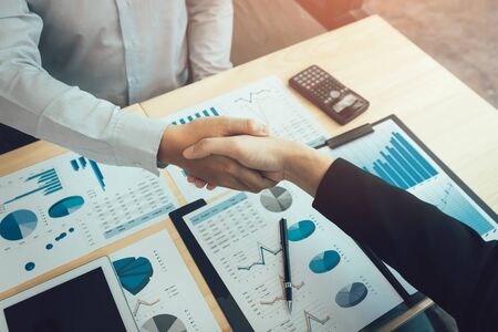 Entrepreneurs collaboration deal shaking hands in a modern office and financial paper graph on desk.の写真素材