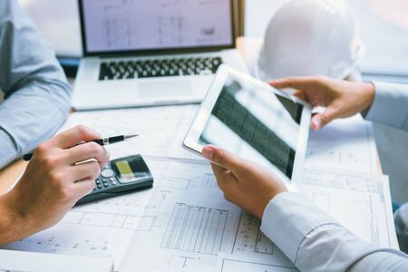 Two engineering working together and using digital tablet looking blueprint and analysis with...