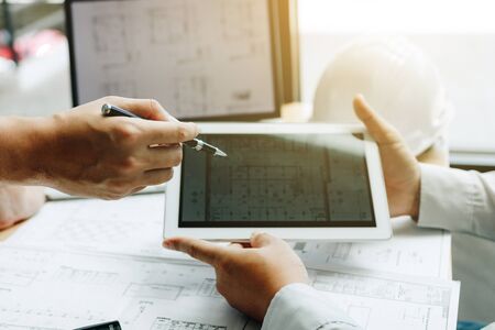 Two engineering working together and using digital tablet looking blueprint and analysis with...