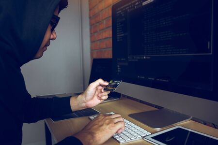 Hacker in the hood working with computer and holding credit card with payment hacking concept.