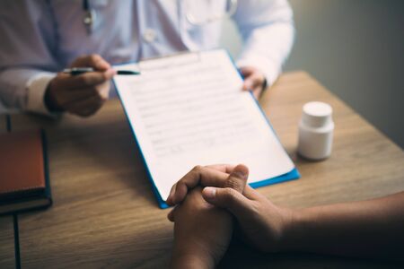 Doctor hand holding pen pointing patient history list on note pad and talking to the patient about medication and treatment.の写真素材