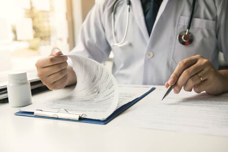 Doctor hand holding pen writing patient history list on note pad and talking to the patient about medication and treatment.の写真素材