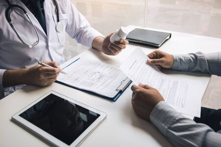 Confident doctor man holding a pill bottle and talking with senior patient and reviewing his medication at office room.の写真素材