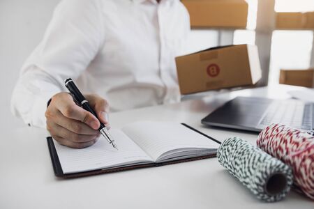 Business owner is checking the product that the customer orders the product pack in the notebook.