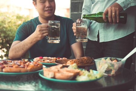Asian friends are pouring beer into the glass while friends are waiting to celebrate in their home.の写真素材
