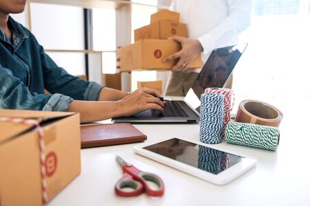 Two business owner are working together to pack products and check customers' orders on their laptops at home.の写真素材