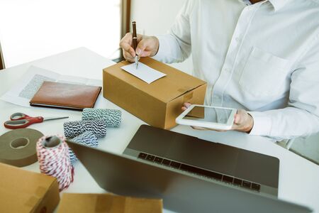 Asian business teenager is looking on tablet and writing a customer address contact to deliver the...